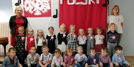 Powiększ grafikę: Dzieci z grupy Pszczółki na tle dekoracji symbolizującej flagę i godło Polski.