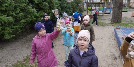 Powiększ grafikę: Dzieci z grupy Słoneczek w ogrodzie przedszkolnym trzymają czekoladowe zajączki. W tle drzewa i piaskownica.