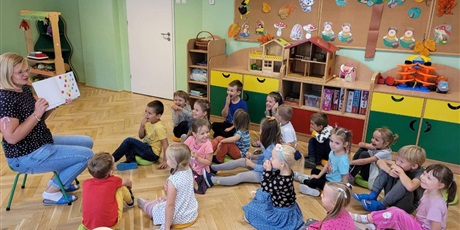 Powiększ grafikę: Dzieci z grupy Motylki siedzą na podłodze. Obok pani Karina pokazuje książkę z kropkami. w tle meble z zabawkami. 