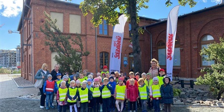 Powiększ grafikę: Dzieci z grupy Słoneczek i Motylków stoją w gromadce. W tle budynek Stoczni Gdańskiej oraz banery z napisem Solidarność