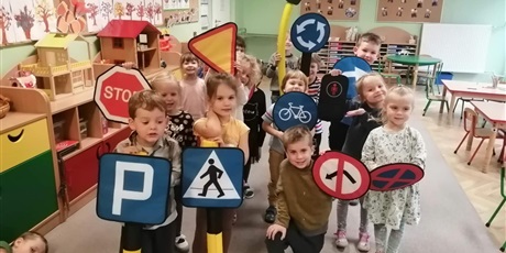 Powiększ grafikę: Dzieci z grupy Motylki stoją w gromadce, trzymają szablony  znaków drogowych. 