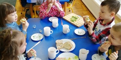 Powiększ grafikę: Dzieci z grupy Pszczółki jedzą kanapki, które same przygotowały. Na stole naczynia sztućce produkty.